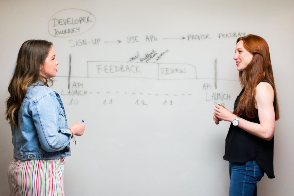 photo-of-women-talking-beside-whiteboard-3861952 Two women engaging in a discussion about API development processes at a whiteboard.